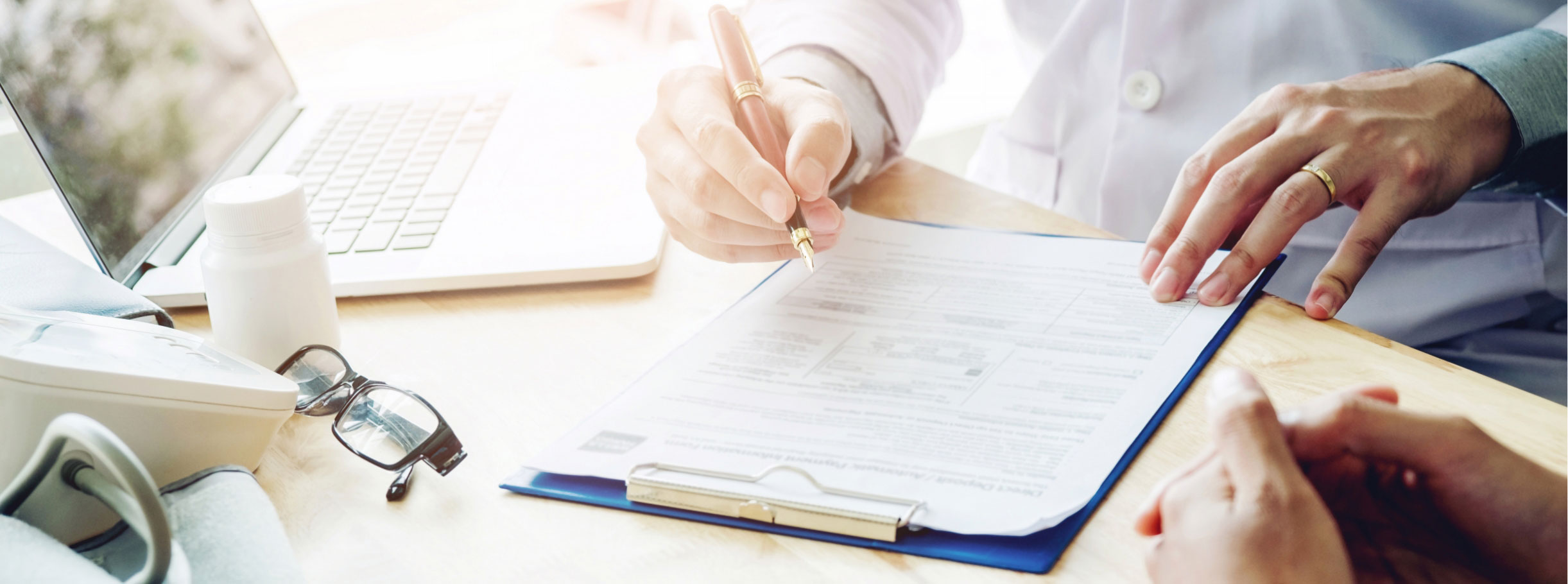Médico tomando notas en consulta frente a un paciente