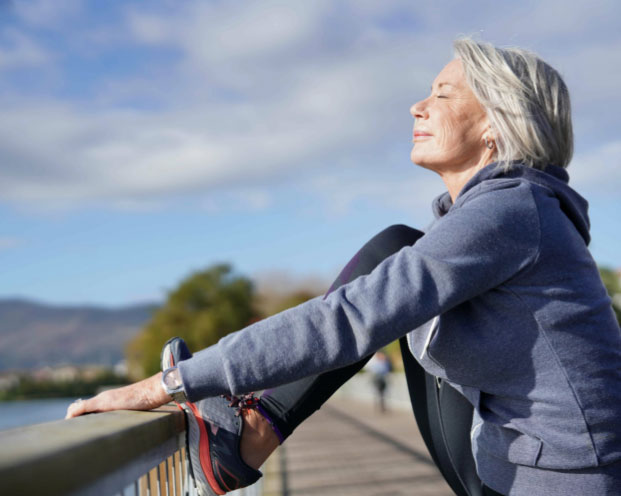 Images de una mujer mayor disfrutando del sol mientras estira para hacer deporte